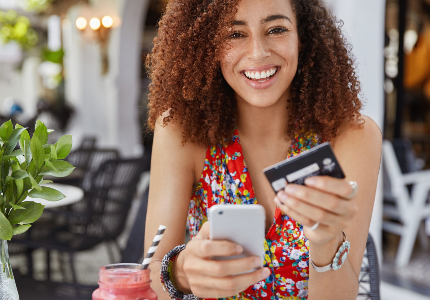 Mulher sorrindo enquanto usa cartão de crédito e celular para pagamentos e controle financeiro