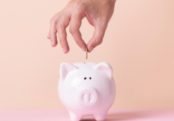 Mano colocando una moneda en una alcancía, representando ahorro y control financiero para evitar deudas.