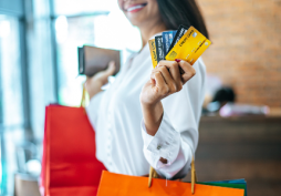 Mulher segurando vários cartões de crédito após compras com sacolas na mão