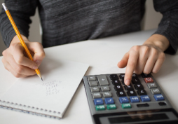 Pessoa fazendo cálculos financeiros com calculadora e anotando valores no caderno