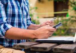Pessoa utilizando cartão de crédito e celular ao lado de um notebook, representando tentativa de pagamento online ou realização de transferência bancária.